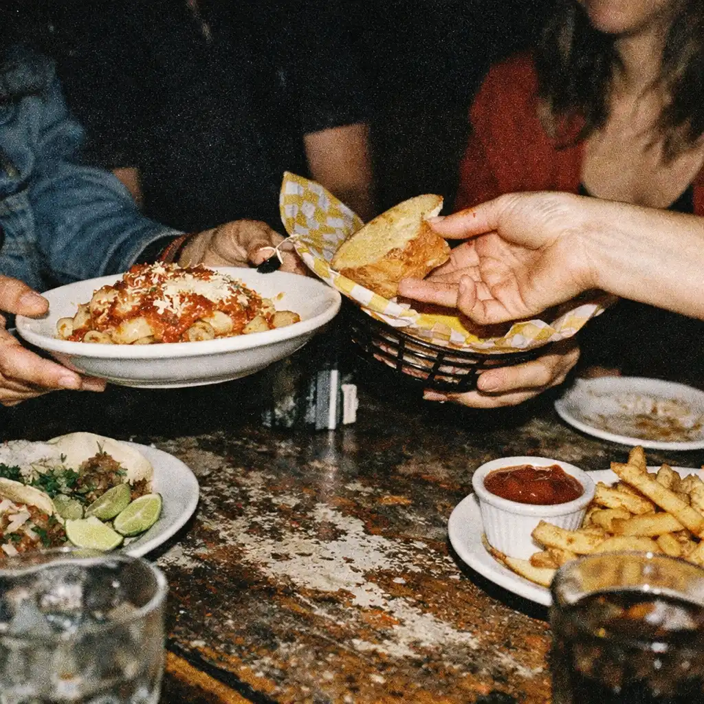 Diners' hands passing food across a worn table at night.