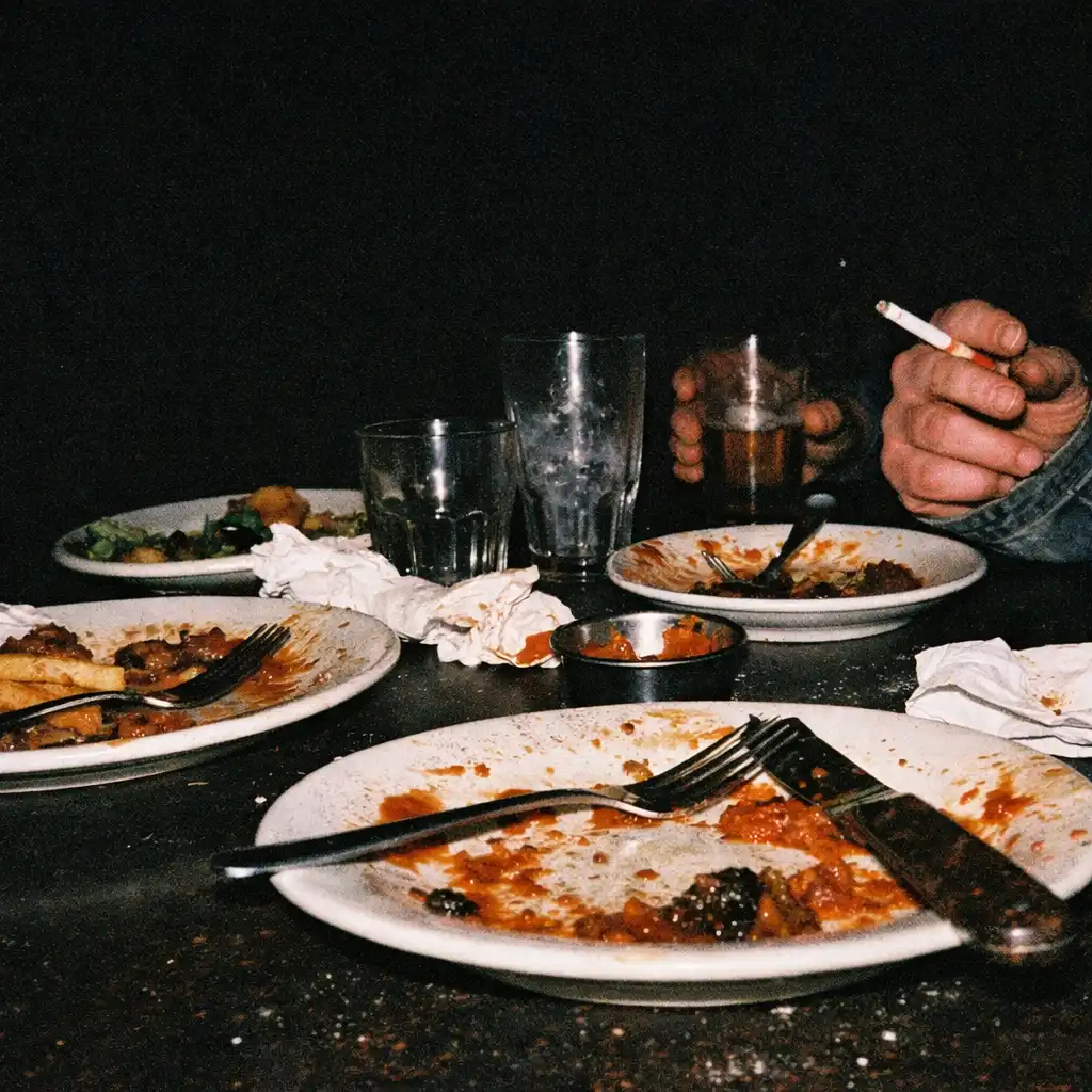 Flash-lit after-hours restaurant table with food, cutlery and diners' hands.