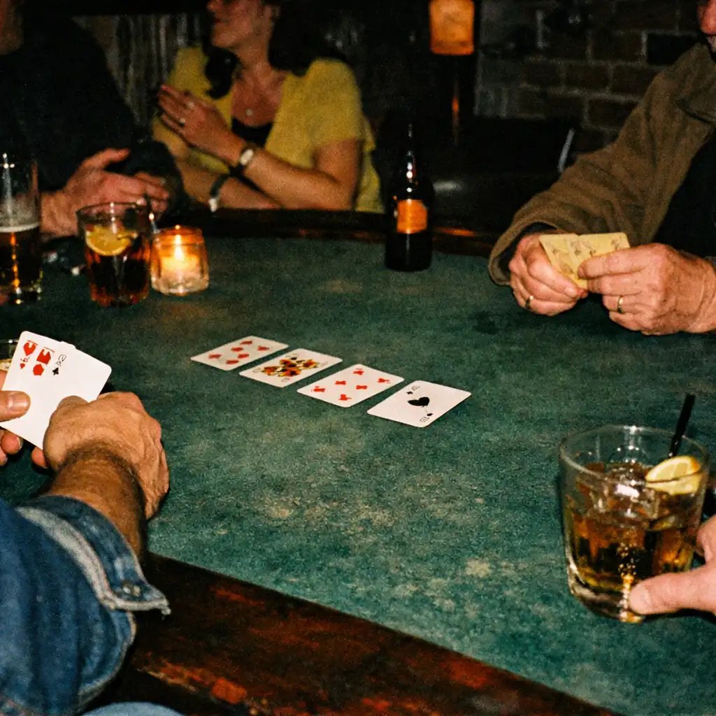 Adult hands, cards, drinks and table texture at a physical social poker table in a dark restaurant venue
