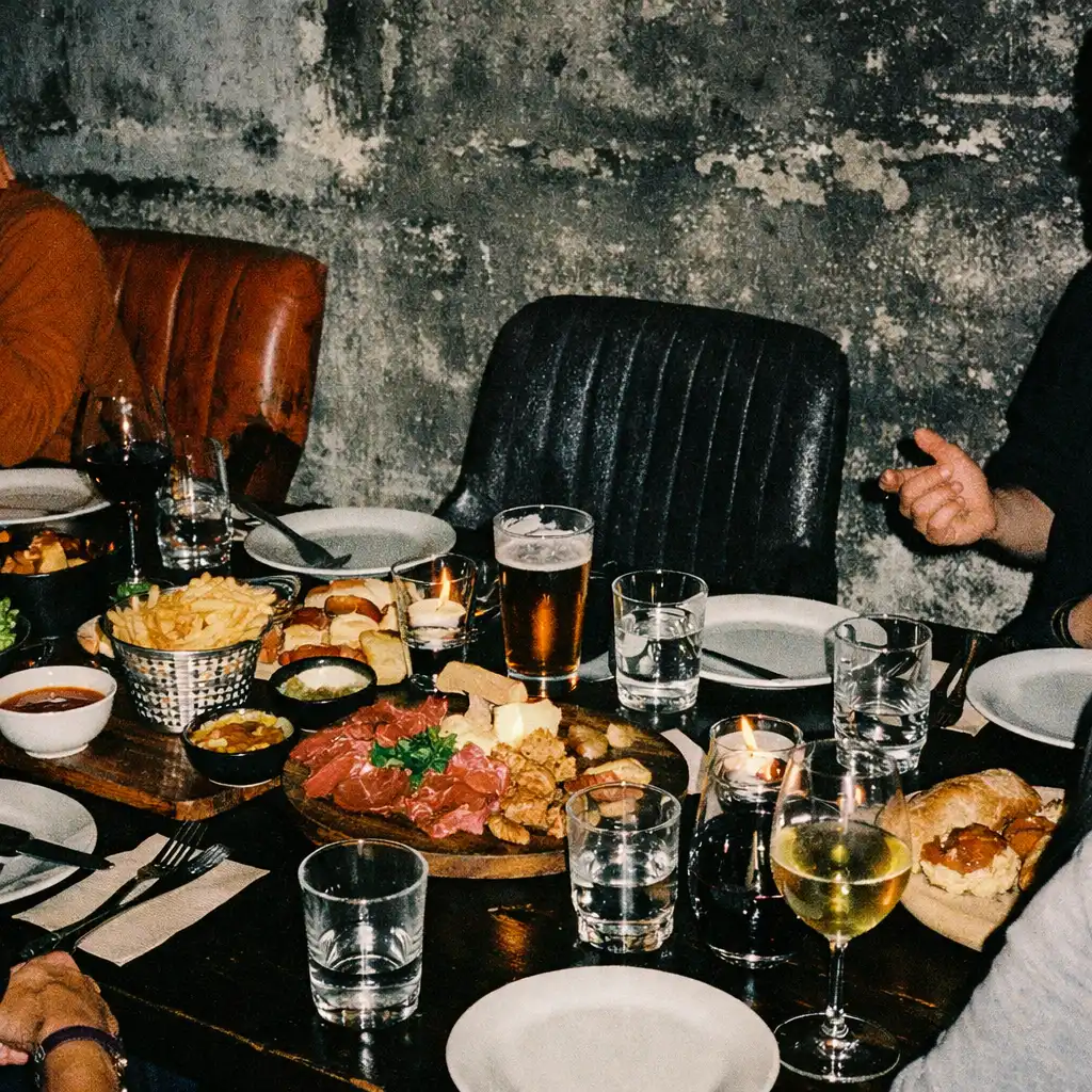 Shared restaurant table set for an informal evening gathering in a dark textured interior